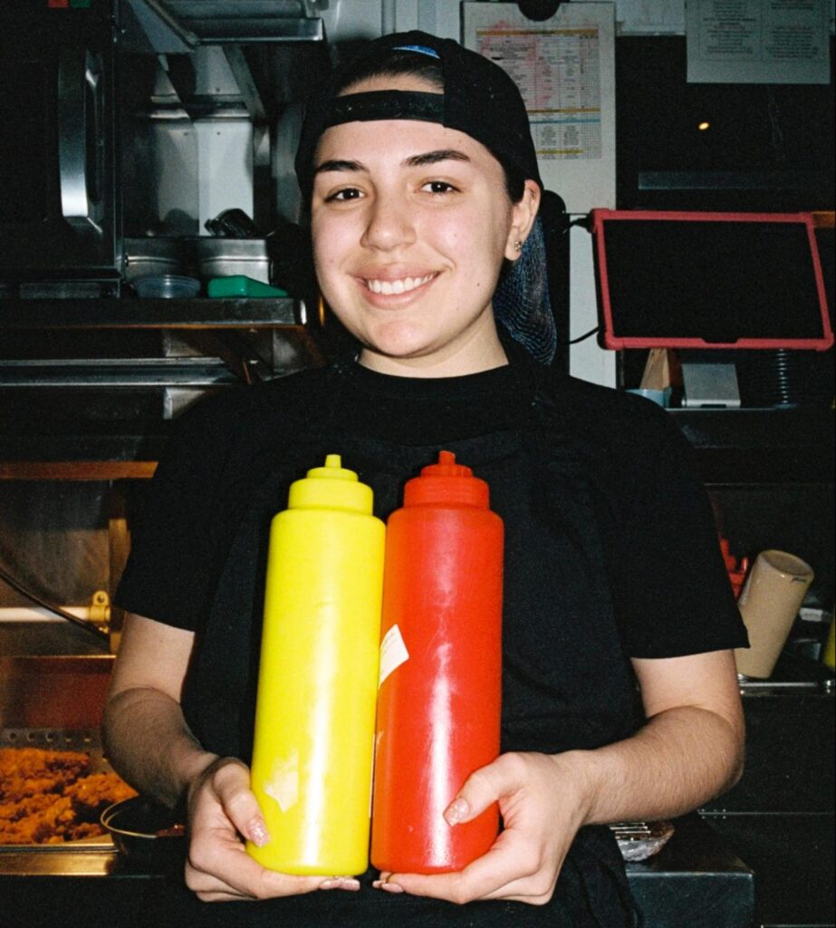 Smiling restaurant worker holding ketchup and mustard
