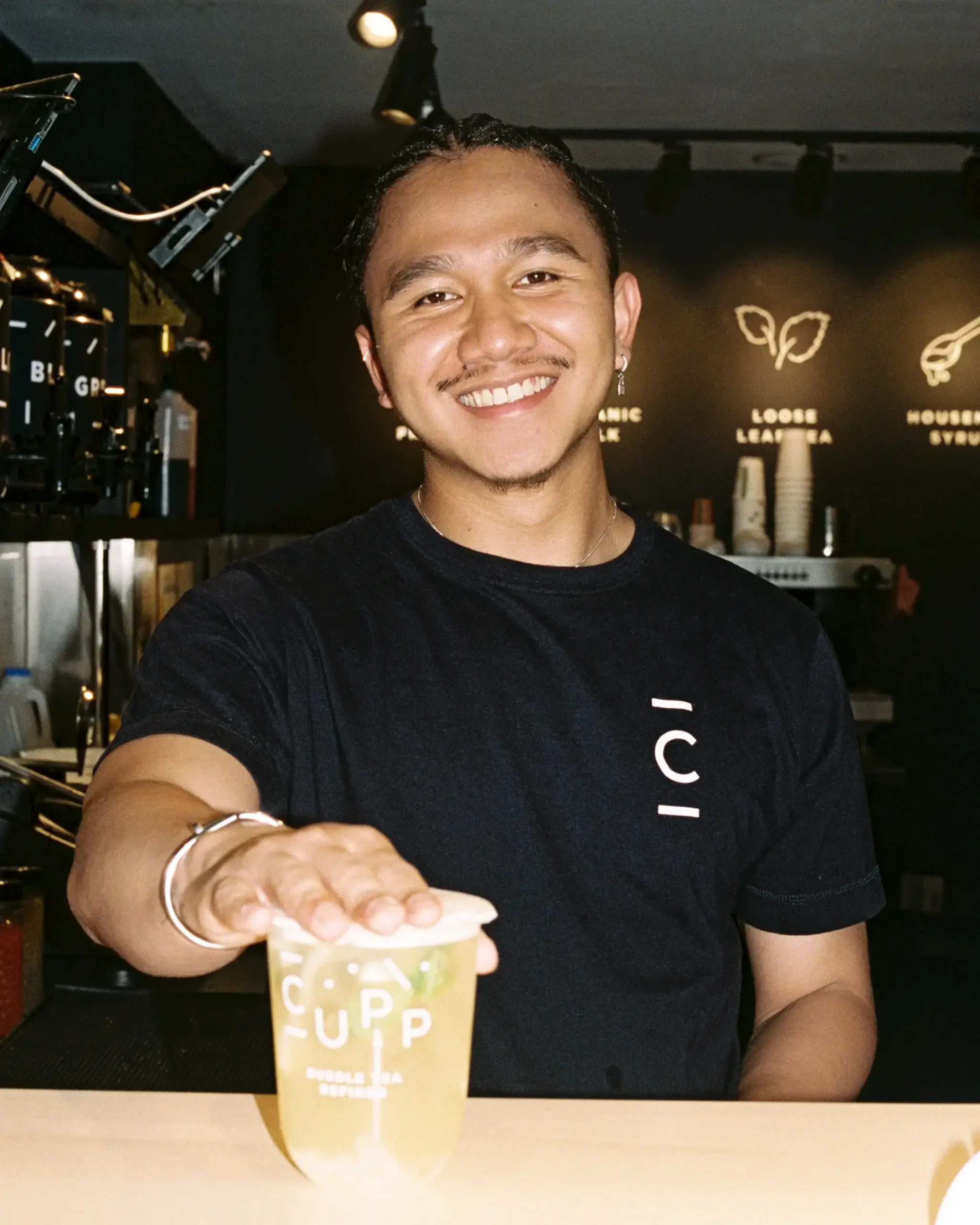 Hospitality employee smiling at the camera and handing a drink to a customer