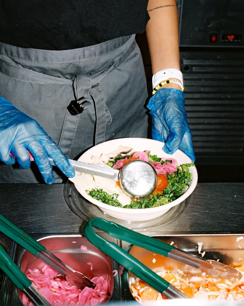Hospitality worker serving healthy food into a takeaway bowl