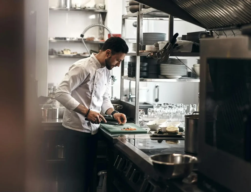 Chef preparing food in a kitchen surrounded by kitchen equipment and crockery