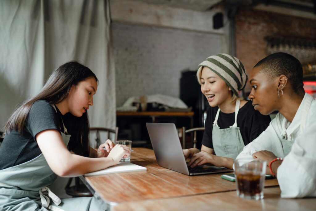 A group of restaurant workers talking at a table with a laptop and notepad